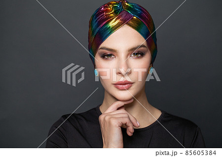 Beautiful stylish woman wearing a headscarf turban and touching her chin while looking at camera Beautiful stylish woman wearing a headscarf turban and touching her chin while looking at camera 85605384