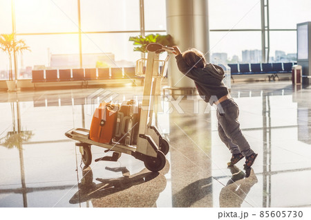 Cute little boy with orange suitcase at airport. The boy on the trolley and the airport Cute little boy with orange suitcase at airport. The boy on the trolley and the airport 85605730
