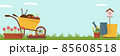 Spring landscape in the garden with green grass, flower, garden wheelbarrow, shovel. 85608518