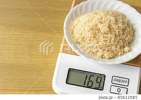 デジタルキッチンスケールで茶色い砂糖（粗糖）を量るイメージ 85612085