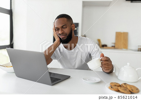 Tired black man using laptop sitting at kitchen table 85621014