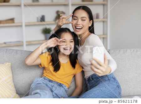 Satisfied teenage girl and young asian female have fun together, make selfie on smartphone Satisfied teenage girl and young asian female have fun together, make selfie on smartphone 85621178