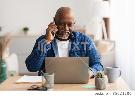 African Male Talking On Phone Using Laptop Sitting In Office 85621200