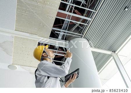 タブレットを持ってビル天井の破損箇所を調査する作業服姿の男性 タブレットを持ってビル天井の破損箇所を調査する作業服姿の男性 85623410
