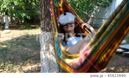 joyful woman wearing virtual reality glasses rests in a hammock near a tree, imagining a dream come joyful woman wearing virtual reality glasses rests in a hammock near a tree, imagining a dream come 85623690