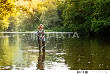 A woman stands in the river and fishes with a spinning rod 85628765
