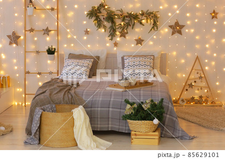 Christmas decorated bedroom with garlands, stars, xmas tree, ladder, presents and bed close up photo 85629101