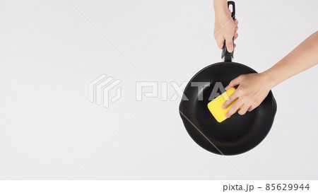 Cleaning Electric non stick pan. Hand on white background cleaning the non stick pan with handy dish washing sponge which yellow color on the soft side and green on hard side for hygiene after cook. Cleaning Electric non stick pan. Hand on white background cleaning the non stick pan with handy dish washing sponge which yellow color on the soft side and green on hard side for hygiene after cook. 85629944