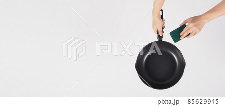 Cleaning Electric non stick pan. Hand on white background cleaning the non stick pan with handy dish washing sponge which yellow color on the soft side and green on hard side for hygiene after cook. Cleaning Electric non stick pan. Hand on white background cleaning the non stick pan with handy dish washing sponge which yellow color on the soft side and green on hard side for hygiene after cook. 85629945
