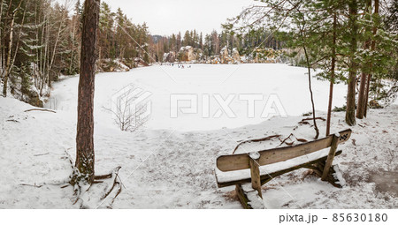 Wooden bench by the frozen blue lake. Winter tracking in popular in Adrspach rocks Wooden bench by the frozen blue lake. Winter tracking in popular in Adrspach rocks 85630180