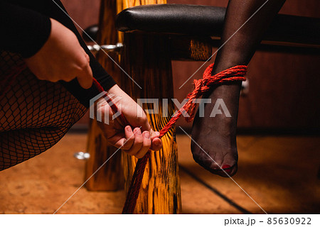 Close-up of female legs in stockings tied with red ropes. 85630922