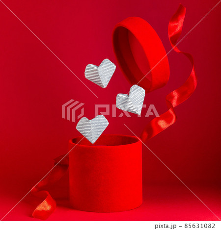 Open flying red velvet box with red silk ribbon, silver hearts fly from box, square format Open flying red velvet box with red silk ribbon, silver hearts fly from box, square format 85631082
