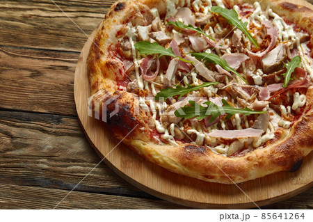 neapolitan Pizza with Mozzarella cheese, bacon, ham, tomato sauce, chicken, Spices and Fresh arugula. Italian pizza on wooden table background 85641264