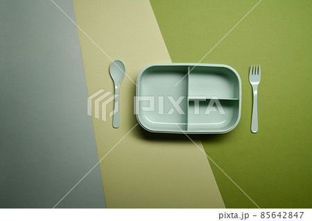 Empty lunch box with spoon and fork on green background. Empty lunch box with spoon and fork on green background. 85642847