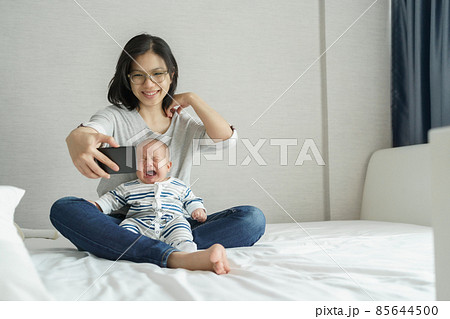 Asian Mother comforting or consoling her baby son while doing online video call on smartphone.  85644500