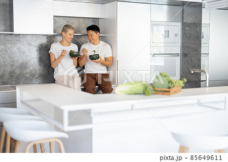 Laughing couple eating salad on kitchen at home Laughing couple eating salad on kitchen at home 85649611
