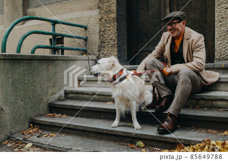 Happy senior man sitting on stairs and resting during dog walk outdoors in city. 85649788