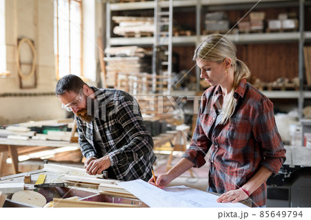 Two carpenters man and woman looking at blueprints indoors in carpentery workshop. 85649794