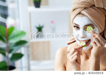 Beautiful young woman with towel wrapped around her head applying face mask at the bathroom 85649959