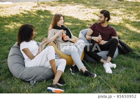 Three friends talking while sitting on the bean bag chairs in a park Three friends talking while sitting on the bean bag chairs in a park 85650952