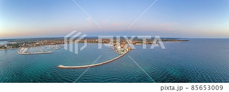 Drone panorama of the Croatian coastal town Umag taken during sunset above the harbor entrance with breakwater Drone panorama of the Croatian coastal town Umag taken during sunset above the harbor entrance with breakwater 85653009