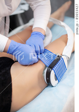 The procedure of myostimulation on the legs of a woman in a beauty salon. 85653427