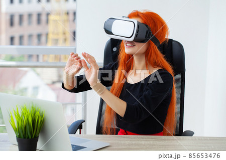 Pretty beautiful cute excited woman in VR headset trying to touch objects in virtual reality Pretty beautiful cute excited woman in VR headset trying to touch objects in virtual reality 85653476