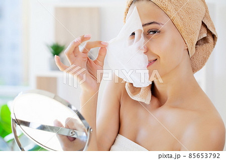 Woman applies white cloth moisturizing mask on her face 85653792