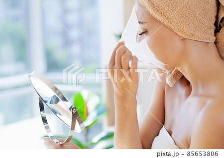 Woman applies white cloth moisturizing mask on her face Woman applies white cloth moisturizing mask on her face 85653806