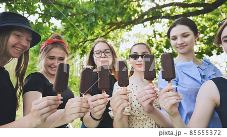 Friends hold chocolate ice cream on a stick in a row. 85655372