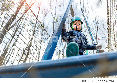 Bottom POV view brave courage little toddler child boy wear safety equipment helmet enjoy passing obstacle course forest rope adventure park on cold winter day. Active outside leisure amusement camp 85656948