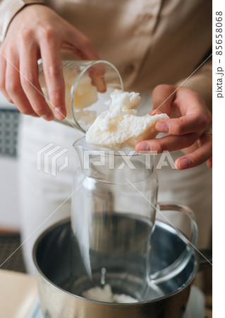 Vertical cropped shot of female artisan adding white dry soy wax in glass jar into pot of boiling water for creating candle building mixture. Vertical cropped shot of female artisan adding white dry soy wax in glass jar into pot of boiling water for creating candle building mixture. 85658068
