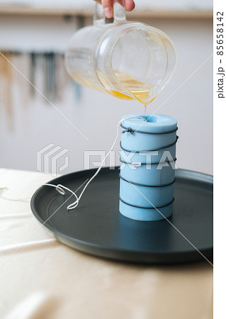 Vertical cropped shot of unrecognizable female artisan pouring yellow liquid wax from glass bowl into silicon mold. 85658142