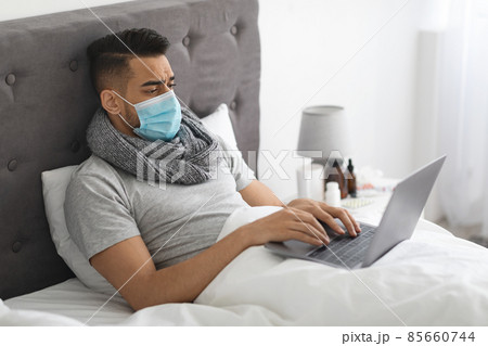Sick Middle Eastern Man In Medical Mask Working With Laptop In Bed Sick Middle Eastern Man In Medical Mask Working With Laptop In Bed 85660744