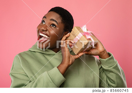 Happy Black Lady Shaking Gift Box Near Ear, Pink Background 85660745