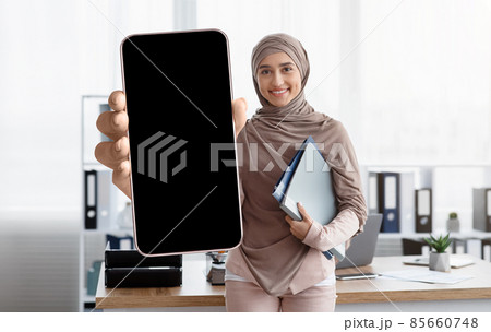 Smiling arab businesswoman showing smartphone with big blank screen, demonstrating device with black touchscreen Smiling arab businesswoman showing smartphone with big blank screen, demonstrating device with black touchscreen 85660748