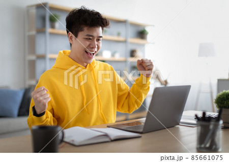 Asian guy using laptop celebrating success shaking fists 85661075