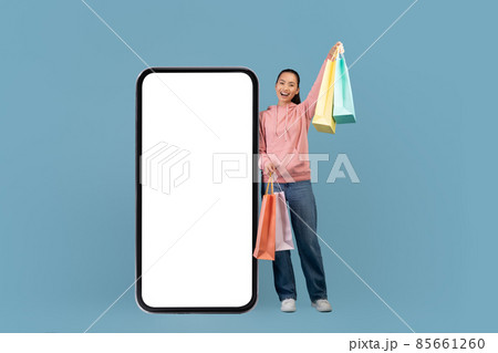 Emotional chinese woman shopaholic with shopping bags and big smartphone Emotional chinese woman shopaholic with shopping bags and big smartphone 85661260