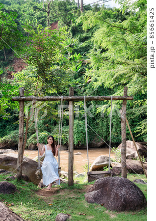 Asian woman in white dress relaxing wooden swing on riverside in the jungle Asian woman in white dress relaxing wooden swing on riverside in the jungle 85661425