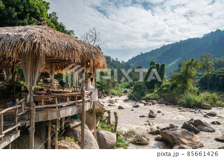 Asian woman relaxing on wooden pavilion as restaurant of tropical resort near the natural rapids in the jungle Asian woman relaxing on wooden pavilion as restaurant of tropical resort near the natural rapids in the jungle 85661426