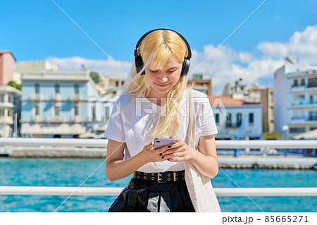 Teenage female in headphones with smartphone on the embankment Teenage female in headphones with smartphone on the embankment 85665271