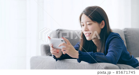 ソファに寝転がってスマホを見る女性 85671745