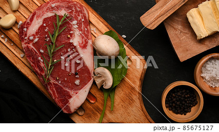 Raw beef steak on top with rosemary and seasoning on a wooden board Raw beef steak on top with rosemary and seasoning on a wooden board 85675127