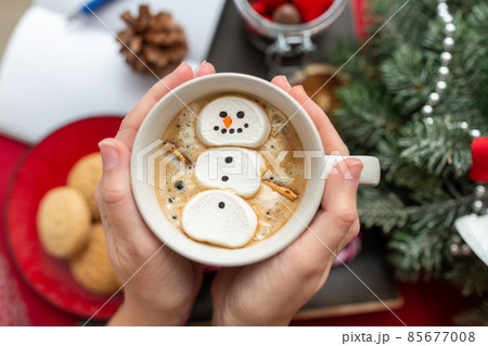 hands with marshmallow snowman in mug on christmas 85677008