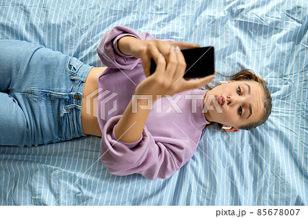 girl in earphones with smartphone lying on bed 85678007