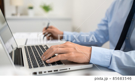 Working Man Conept The male officer sitting in the office, laying his left hand on the laptop, and writing something on the paper with his right hand 85683546