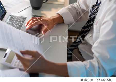Overwork Concept The office personnel in the loose tie sitting at his desk, reading a paperwork and typing on the notebook Overwork Concept The office personnel in the loose tie sitting at his desk, reading a paperwork and typing on the notebook 85683561