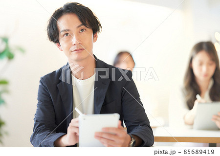 教室の席に座ってタブレットでノートを取る若い男性 85689419