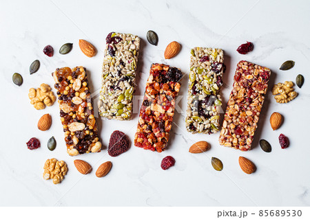 Energy granola bars with different seeds, nuts and dried fruits and berries on white marble background. Healthy snack concept. Energy granola bars with different seeds, nuts and dried fruits and berries on white marble background. Healthy snack concept. 85689530