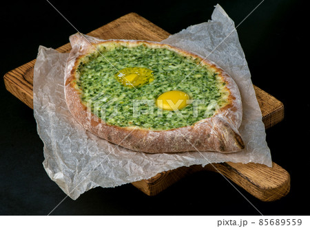 Georgian khachapuri with egg and cheese national traditional cuisine on a black plate on wooden background. Georgian khachapuri with egg and cheese national traditional cuisine on a black plate on wooden background. 85689559